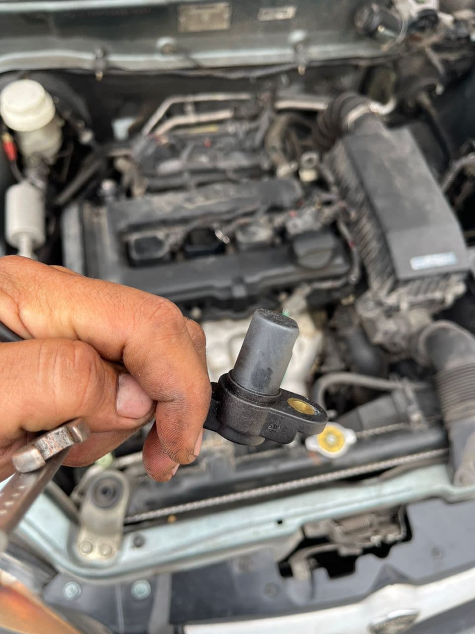 NexFleet vendor mechanic holding camshaft sensor next to open engine bay on a KL job