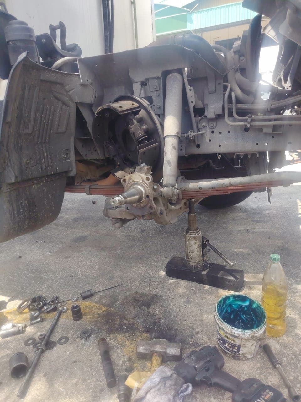 Lorry brake and suspension repair in progress with hydraulic jack, tools, and grease bucket